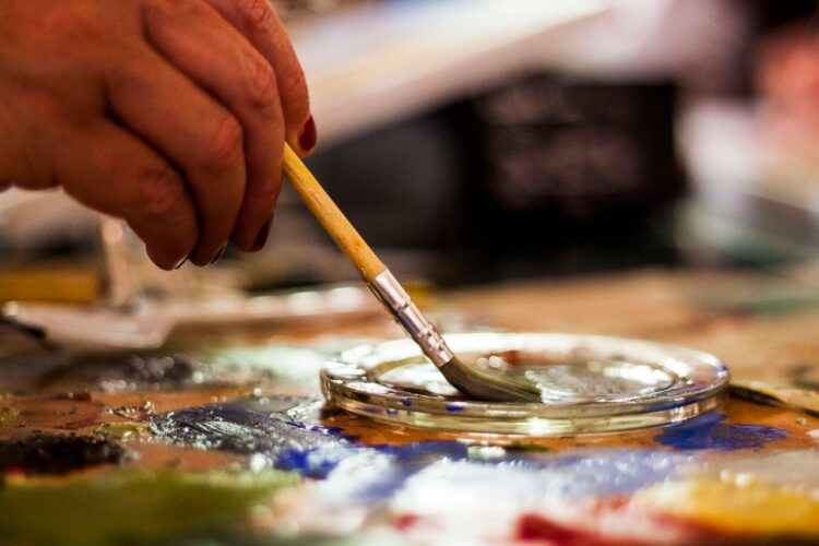 A detailed view of an artist's hand using a paintbrush in a creative indoor setting.