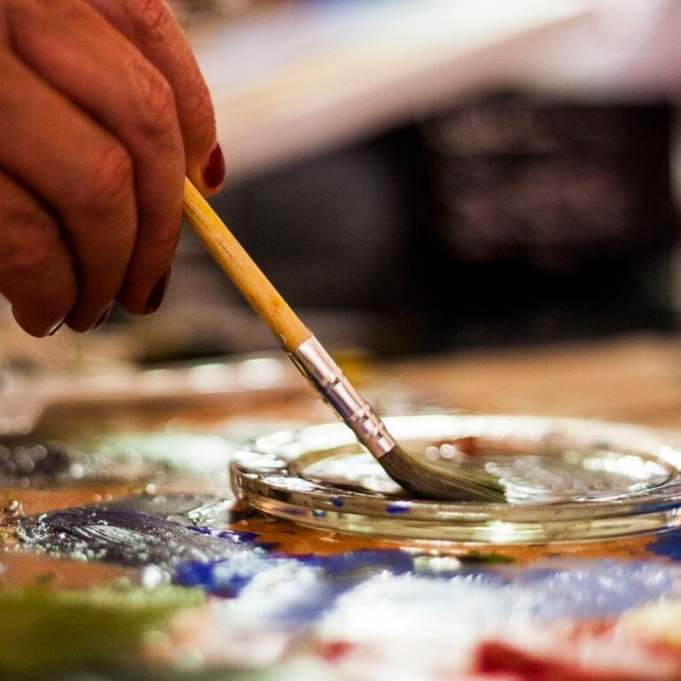 A detailed view of an artist's hand using a paintbrush in a creative indoor setting.