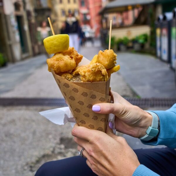 Fried Cod Person holding fried snacks in a paper cone outdoors on a street.