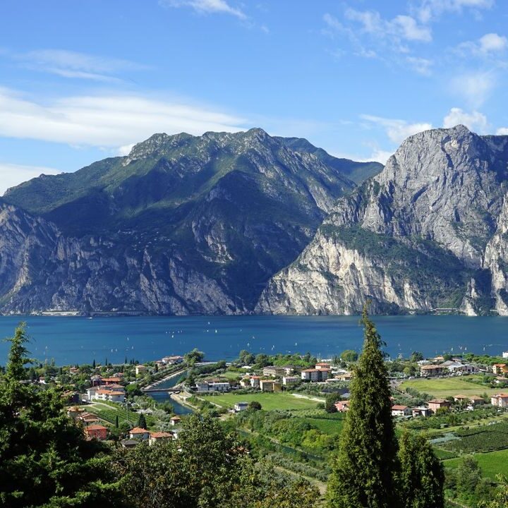 Scenic view of Lake Garda with surrounding mountains and lush green trees in the foreground.