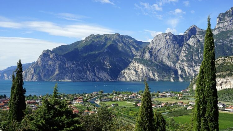 Scenic view of Lake Garda with surrounding mountains and lush green trees in the foreground.