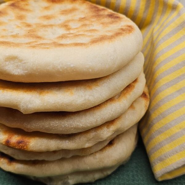 Tigelle Fresh homemade flatbreads stacked with a striped cloth on a green surface. Perfect for culinary use.