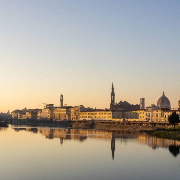 Peaceful sunset view of Florence skyline with the Arno River reflecting historic architecture.
